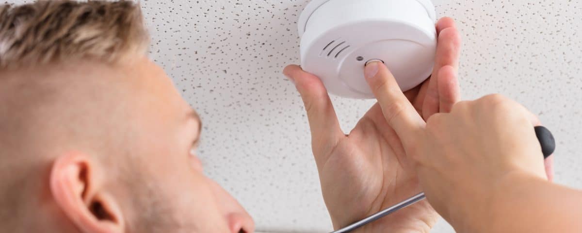 A Person's Hand Installing Smoke Detector On Ceiling Wall At Home