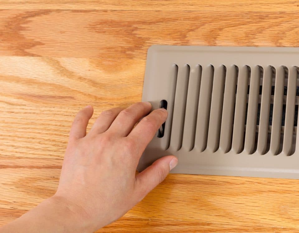 Female hand opening up heater floor vent with Red Oak Floors