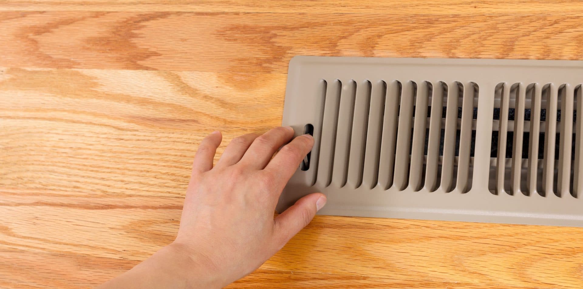 Female hand opening up heater floor vent with Red Oak Floors