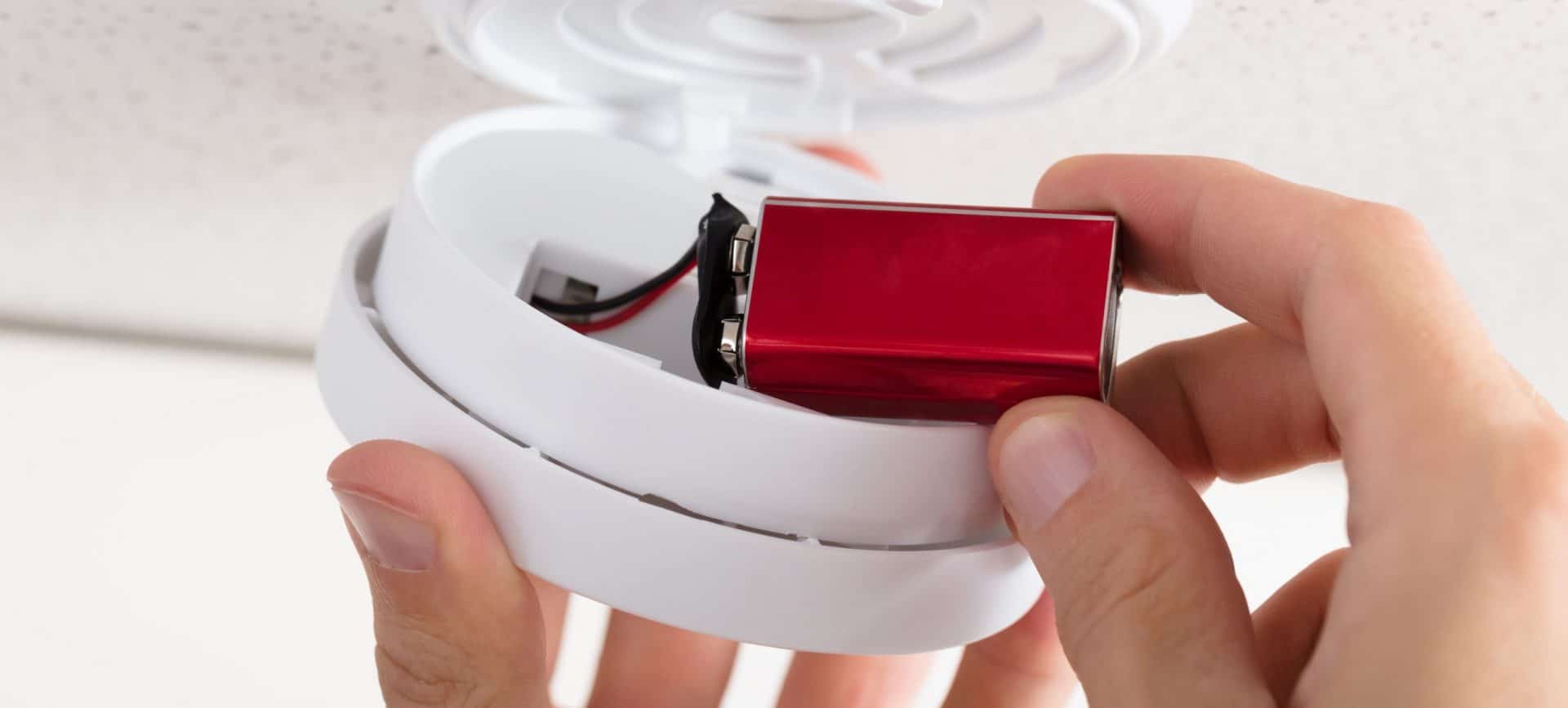 Close-up Of A Person's Hand Inserting Battery In Smoke Detector