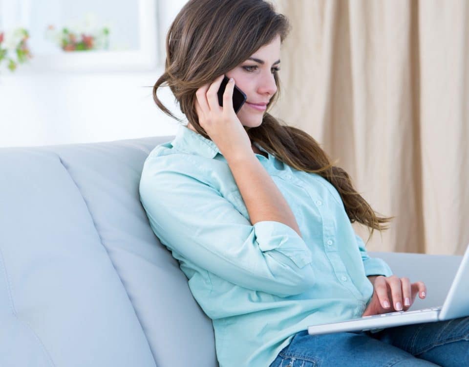 Woman on the phone using her laptop at home in the living room