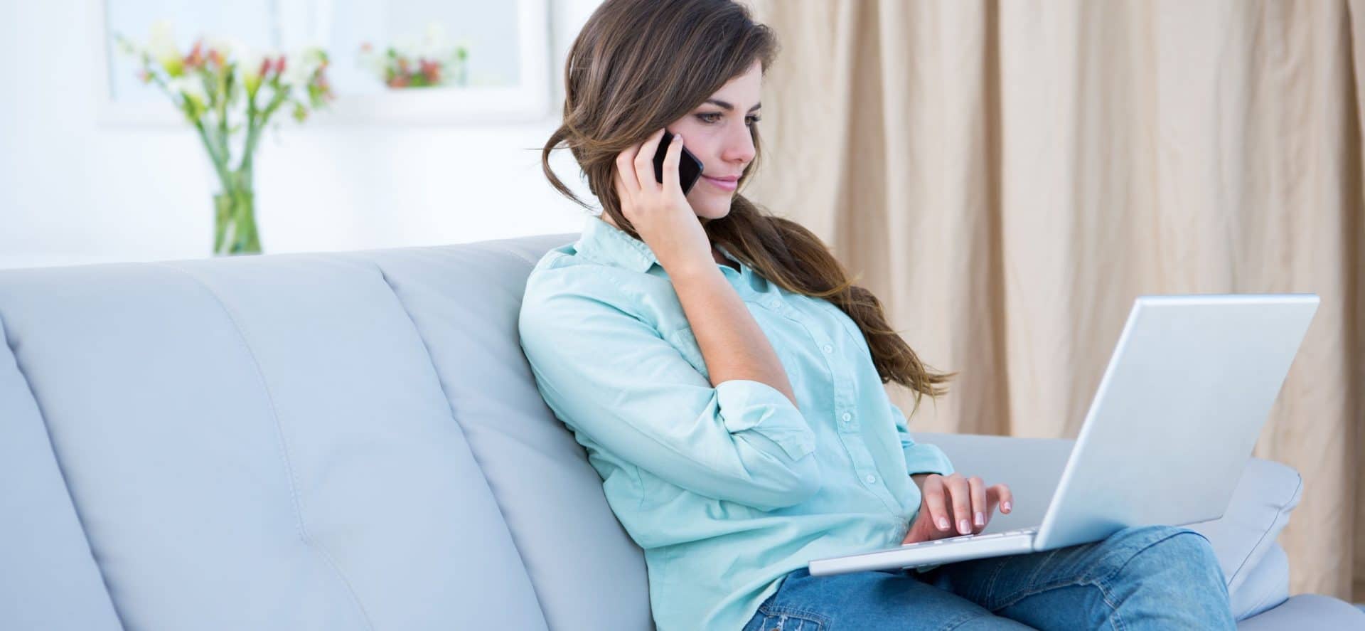 Woman on the phone using her laptop at home in the living room