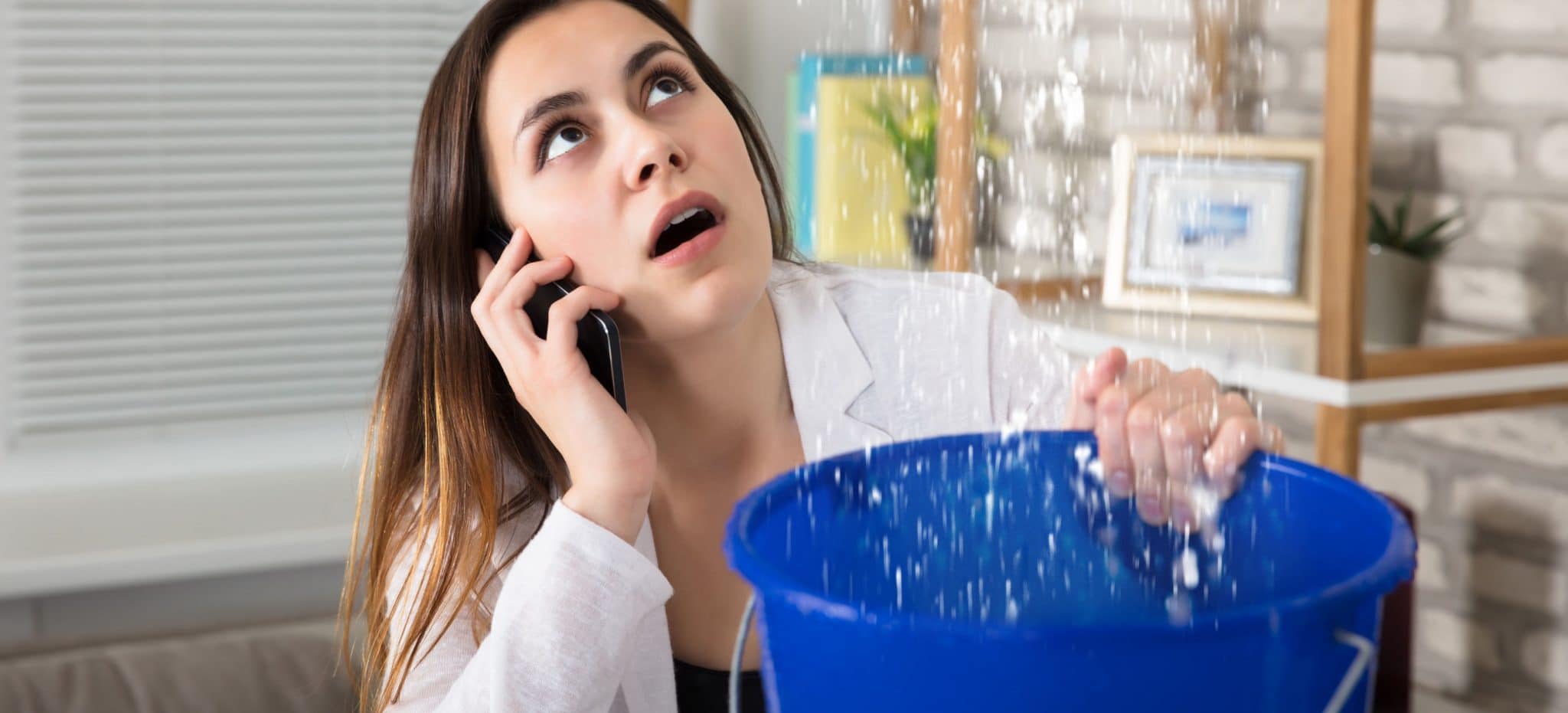 Woman holding bucket under leaking ceiling