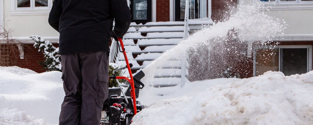 Man blowing snow and clearing the entrance of a house after a winter storm