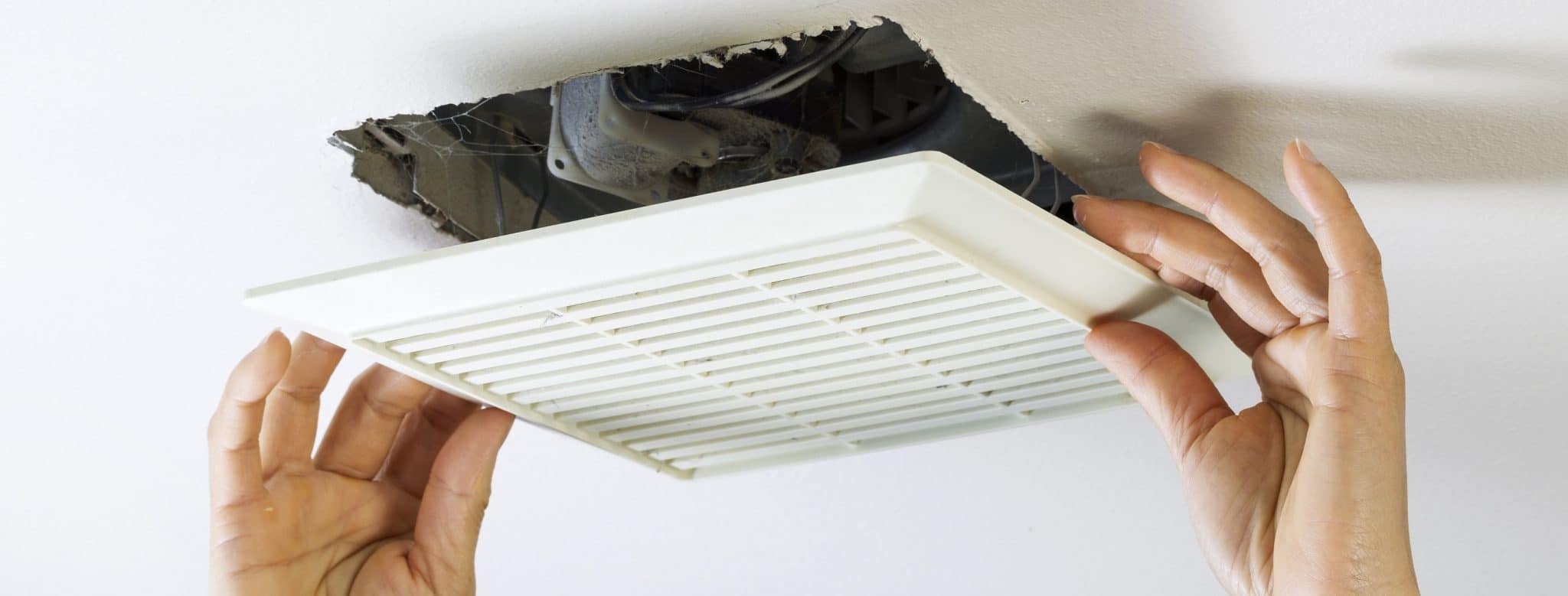 Hands removing vent cover from bathroom ceiling fan