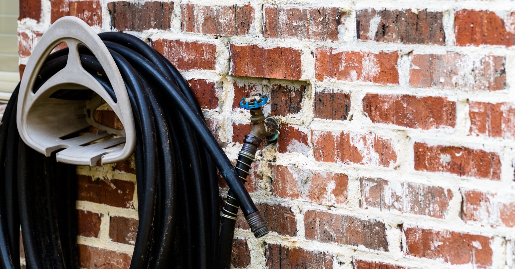 Rubber hose hanging on a brick wall attached to a spigot