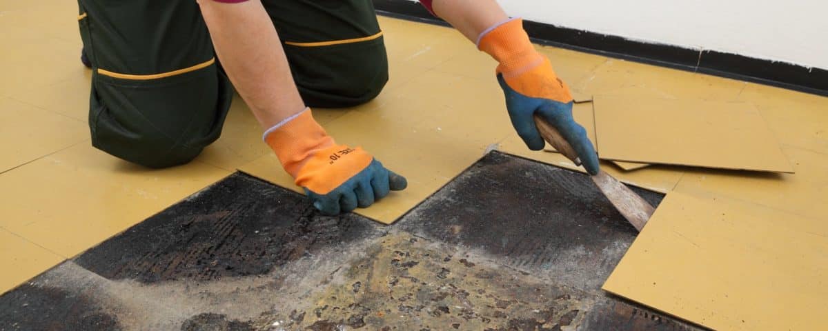 Female worker removing old vinyl tiles from kitchen floor using spatula trowel tool