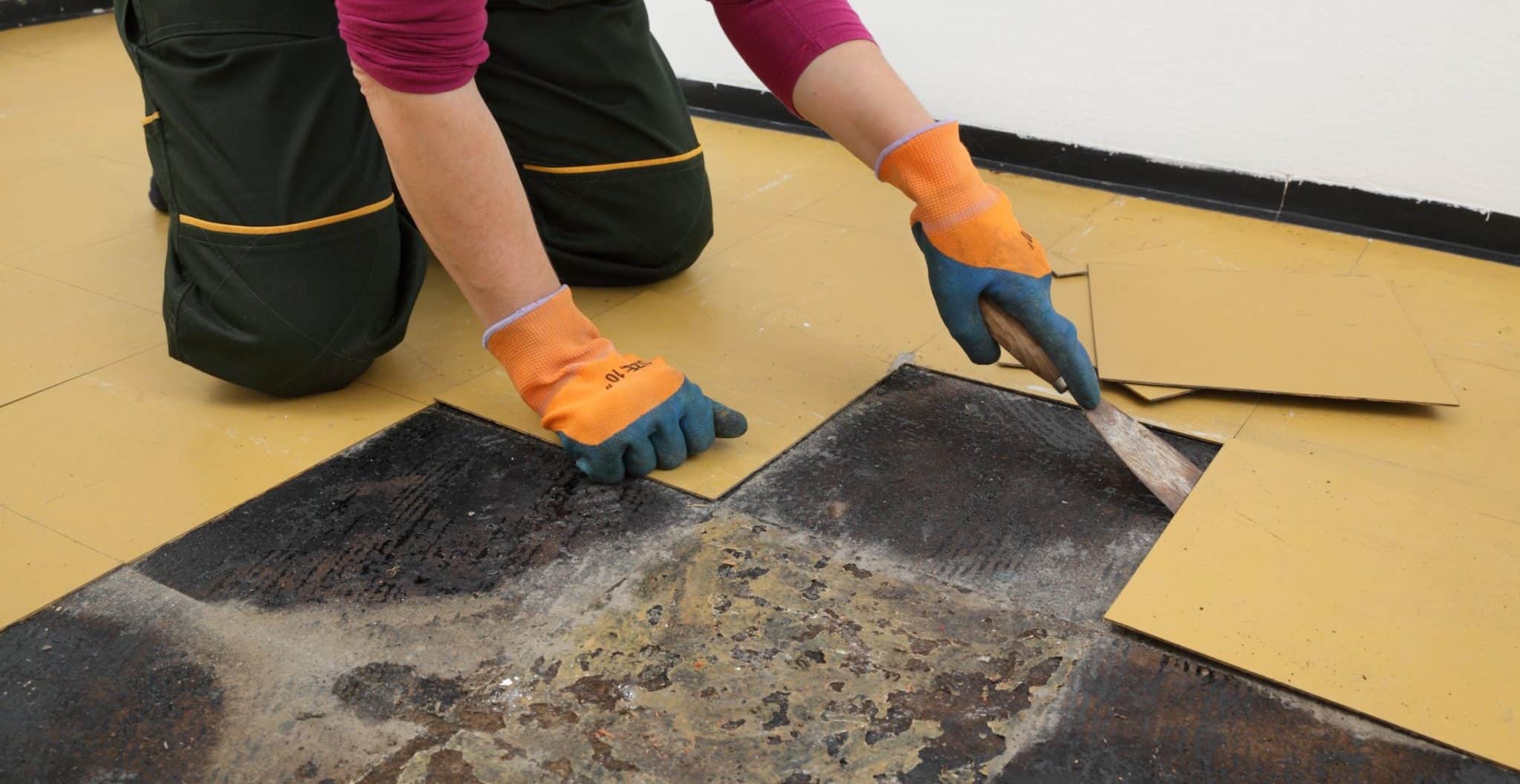 Female worker removing old vinyl tiles from kitchen floor using spatula trowel tool