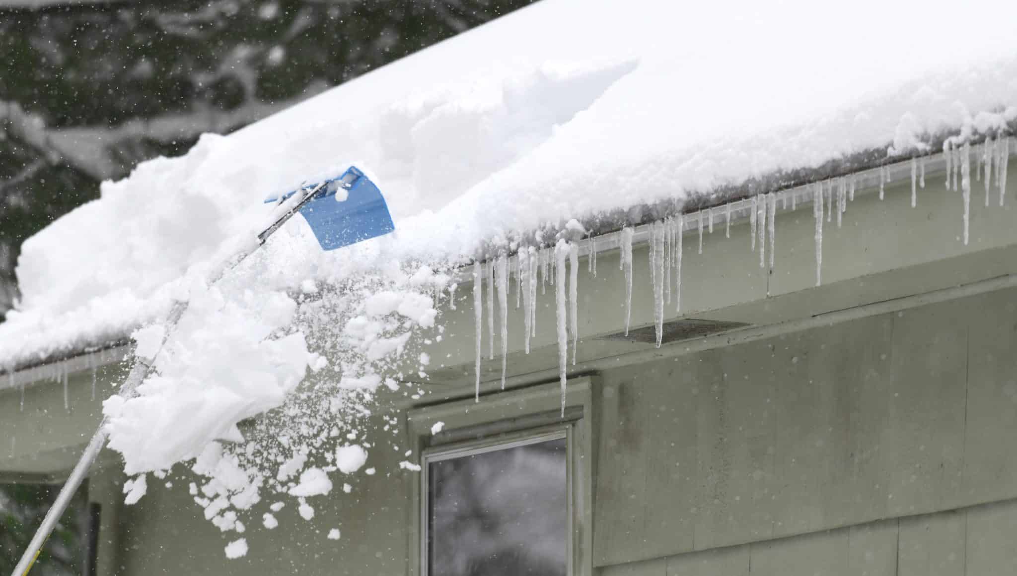 Person removing snow from the roof of a home