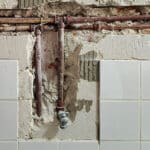 Tile surface of a wall broken away to expose plumbing