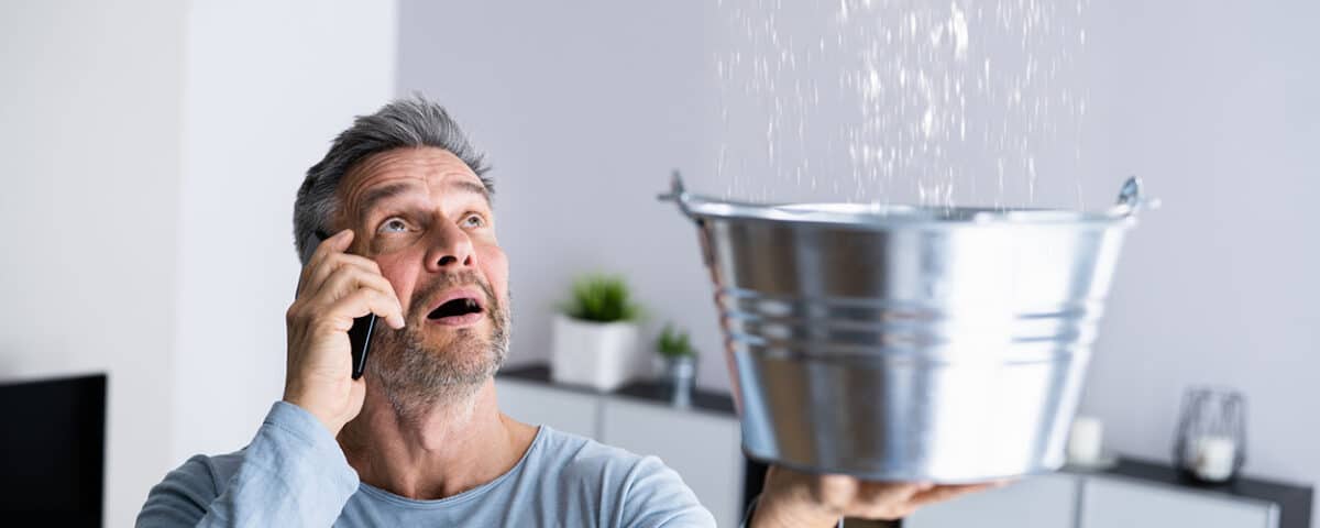 Man catching water leaking from a ceiling in a bucket