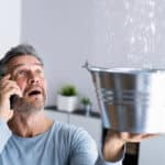 Man catching water leaking from a ceiling in a bucket