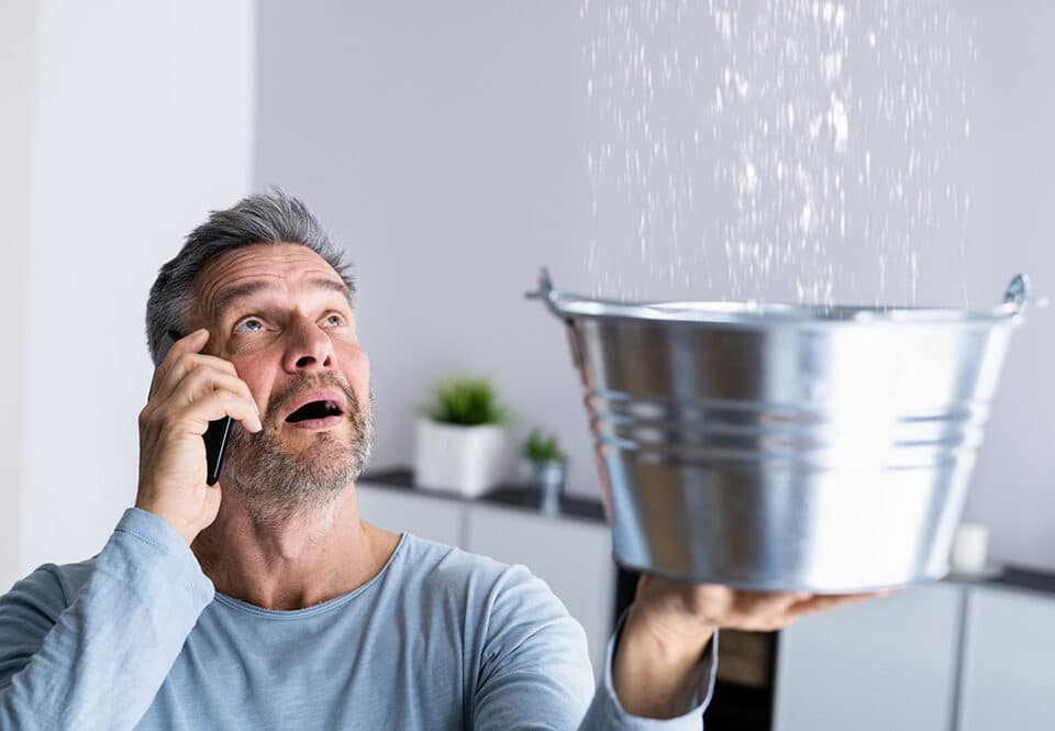 Man catching water leaking from a ceiling in a bucket